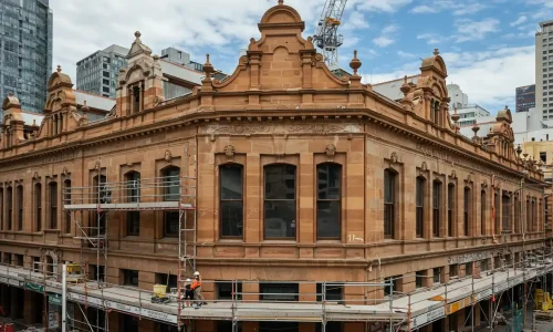 Close-up of a sandstone building with detailed windows and decorative features, scaffolding on the side.