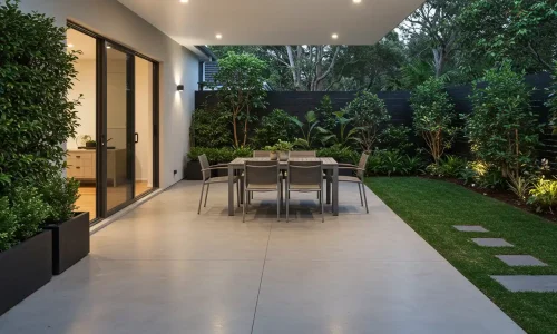 Modern outdoor dining area with a concrete floor, sleek table, and surrounded by greenery and plants, under soft lighting